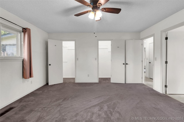 unfurnished bedroom featuring a spacious closet, a textured ceiling, visible vents, ceiling fan, and carpet