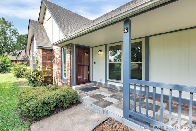 view of exterior entry with a yard, brick siding, a shingled roof, and covered porch