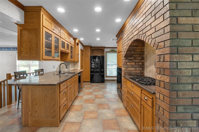 kitchen featuring backsplash, a breakfast bar area, black appliances, dark stone counters, and sink