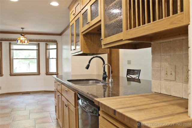 kitchen with hanging light fixtures, crown molding, dark stone counters, stainless steel dishwasher, and sink