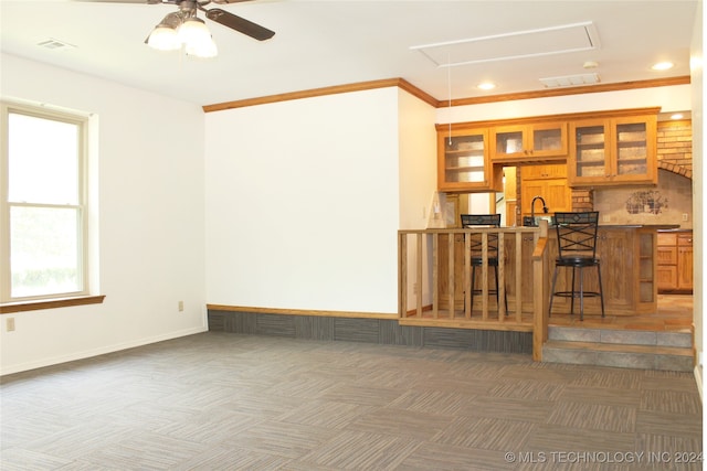 kitchen featuring dark carpet, ceiling fan, kitchen peninsula, a kitchen breakfast bar, and crown molding