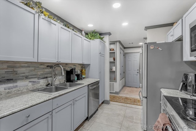 kitchen with sink, backsplash, appliances with stainless steel finishes, light tile patterned floors, and light stone countertops