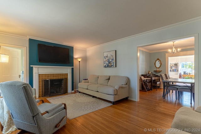 living room featuring an inviting chandelier, crown molding, a tiled fireplace, and hardwood / wood-style floors