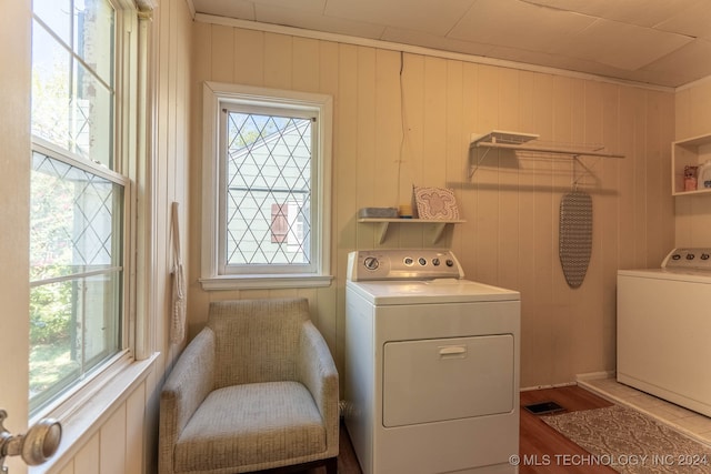 laundry room with light wood-type flooring, wood walls, and washing machine and dryer