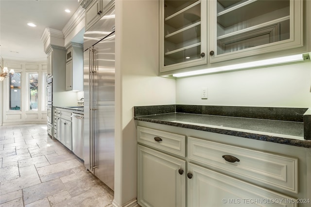 kitchen featuring dark stone countertops, stainless steel appliances, an inviting chandelier, cream cabinets, and sink