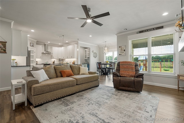 living room featuring ceiling fan with notable chandelier, wood-type flooring, sink, and crown molding