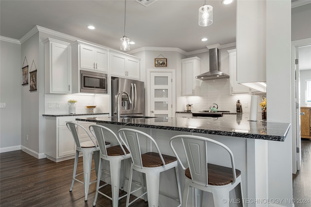 kitchen featuring white cabinetry, dark stone counters, wall chimney range hood, and stainless steel appliances