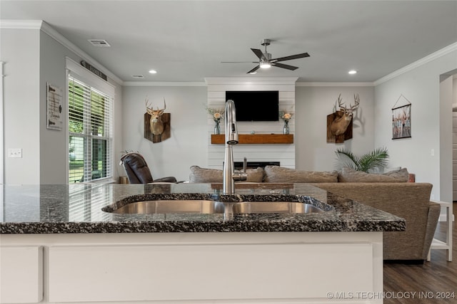 kitchen featuring ceiling fan, dark wood-type flooring, a large fireplace, dark stone counters, and crown molding