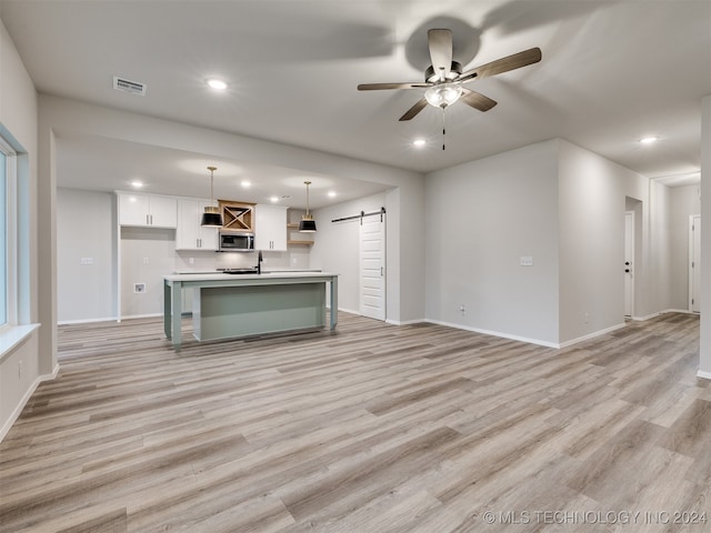 unfurnished living room featuring a barn door, ceiling fan, sink, and light wood-type flooring