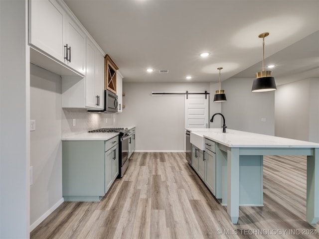 kitchen featuring stainless steel appliances, white cabinetry, light hardwood / wood-style flooring, a barn door, and pendant lighting