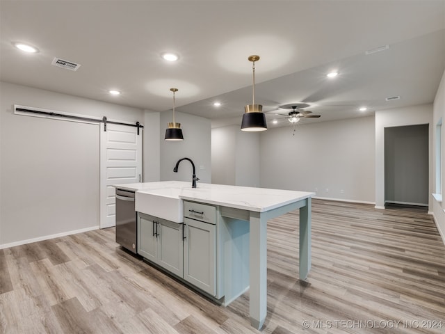 kitchen featuring light stone countertops, a kitchen island with sink, light hardwood / wood-style flooring, a barn door, and pendant lighting