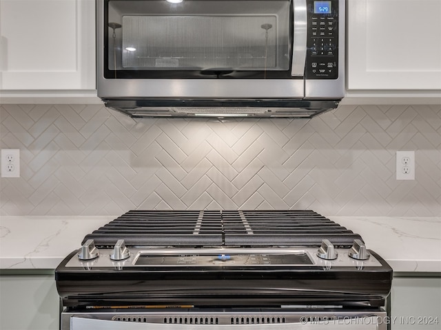 interior details featuring white cabinets, light stone countertops, range, and decorative backsplash