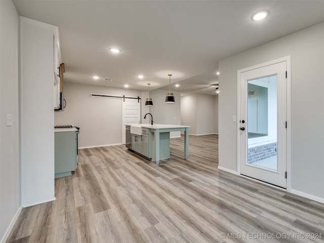 kitchen featuring light hardwood / wood-style floors, a center island with sink, a breakfast bar, decorative light fixtures, and a barn door