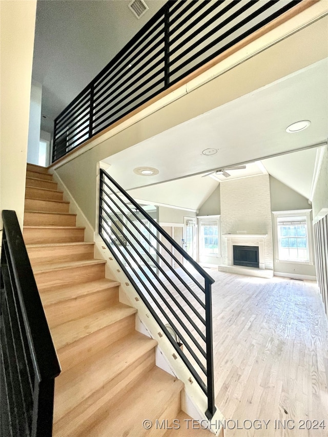 stairs with a large fireplace, vaulted ceiling, and hardwood / wood-style flooring