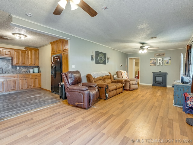 living room with light wood-type flooring, a textured ceiling, sink, ornamental molding, and ceiling fan