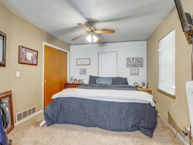 carpeted bedroom featuring ceiling fan, a textured ceiling, a closet, and wood walls