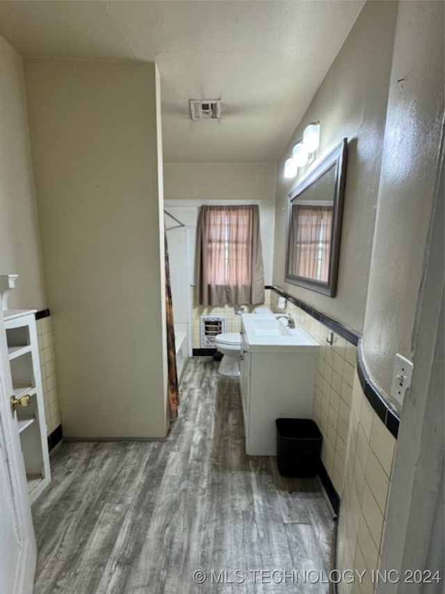 bathroom with tile walls, heating unit, vanity, toilet, and hardwood / wood-style floors