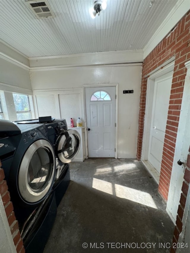 washroom with washing machine and clothes dryer, brick wall, and crown molding