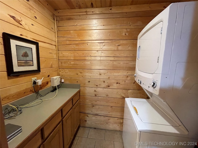 laundry room with wooden walls, wooden ceiling, light tile patterned floors, and stacked washing maching and dryer