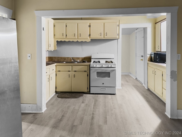 kitchen featuring white range with gas stovetop, stainless steel refrigerator, light hardwood / wood-style floors, and sink