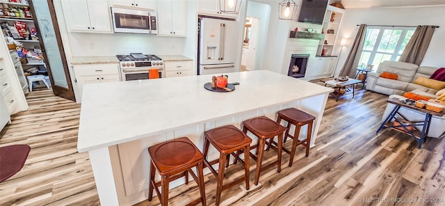 kitchen with light hardwood / wood-style floors, white cabinetry, a breakfast bar, high end appliances, and a kitchen island