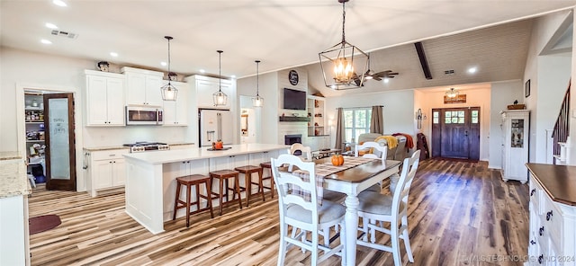 dining room with ornamental molding, a large fireplace, an inviting chandelier, light wood-type flooring, and vaulted ceiling