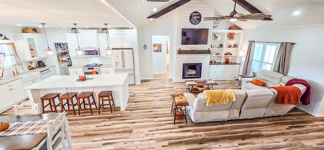 living room with high vaulted ceiling, beamed ceiling, light wood-type flooring, ceiling fan, and sink