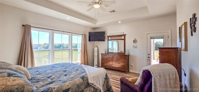 bedroom with ceiling fan, light wood-type flooring, and a tray ceiling