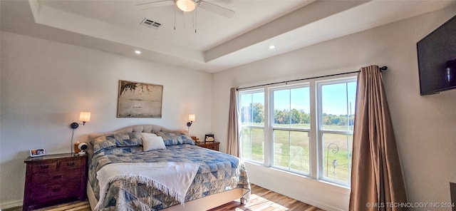 bedroom with ceiling fan, a raised ceiling, hardwood / wood-style floors, and multiple windows