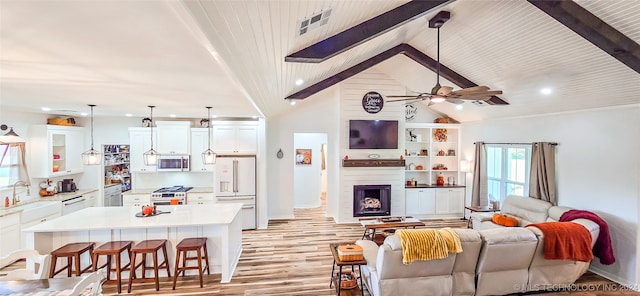 living room with ceiling fan, beam ceiling, light hardwood / wood-style floors, and a large fireplace