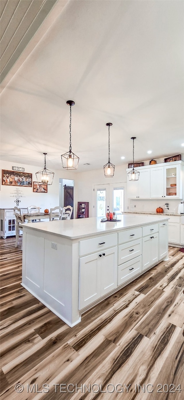 kitchen with hardwood / wood-style flooring, a center island with sink, pendant lighting, and white cabinets