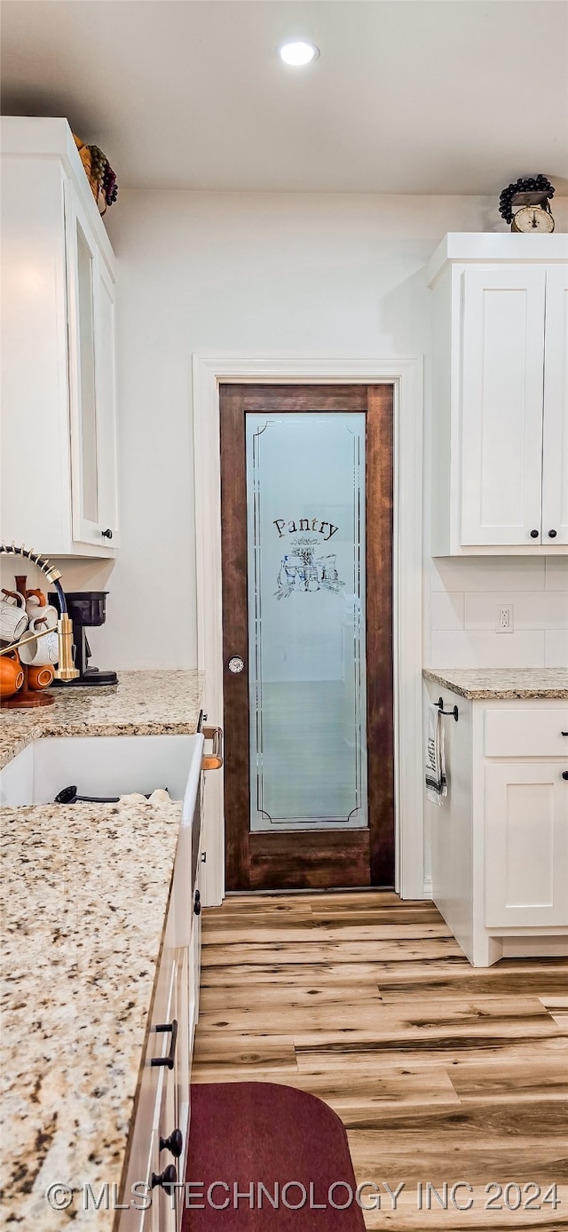 kitchen with sink, light stone countertops, light hardwood / wood-style floors, and white cabinetry