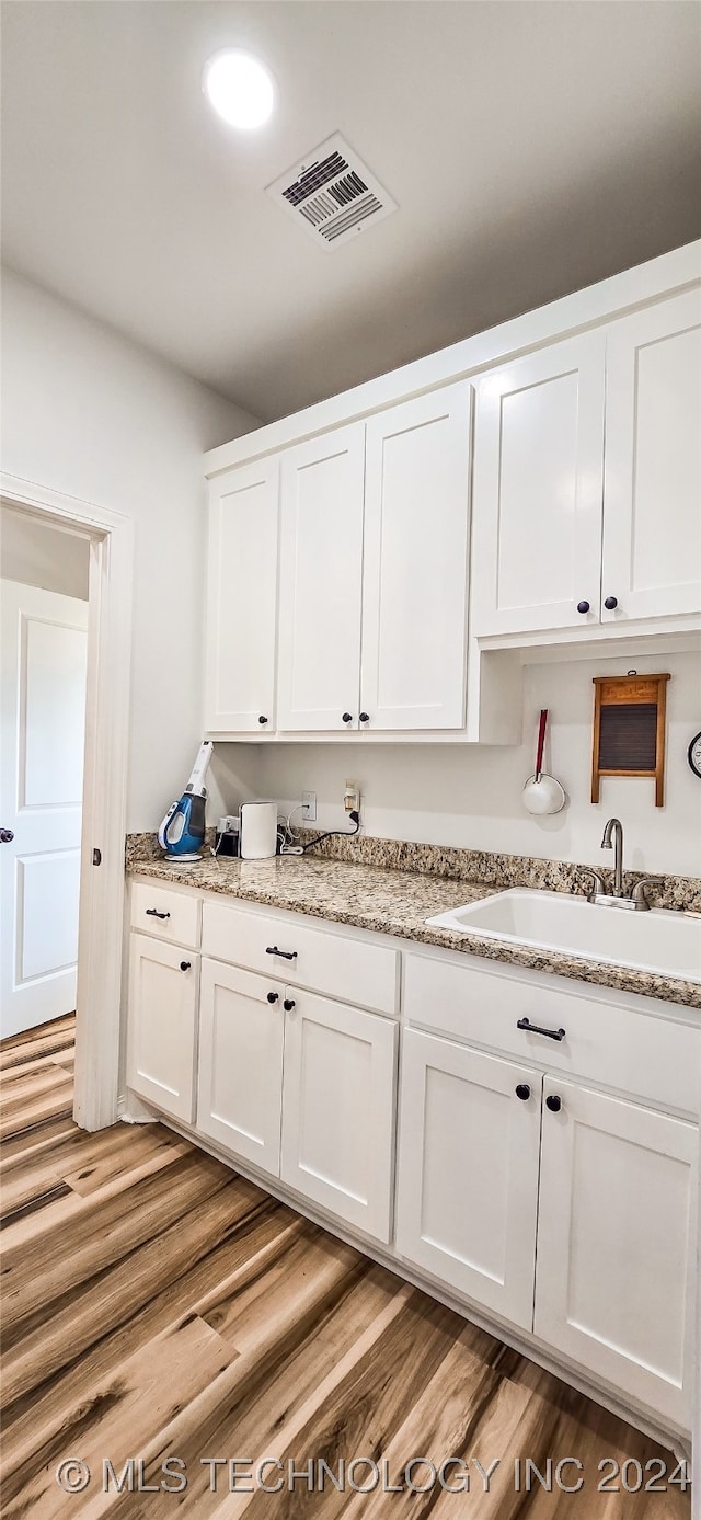 kitchen with light wood-type flooring, white cabinetry, sink, and light stone counters