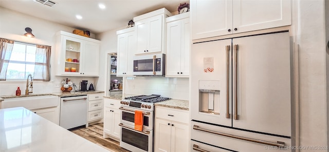 kitchen with white cabinets, sink, high end appliances, light hardwood / wood-style flooring, and backsplash