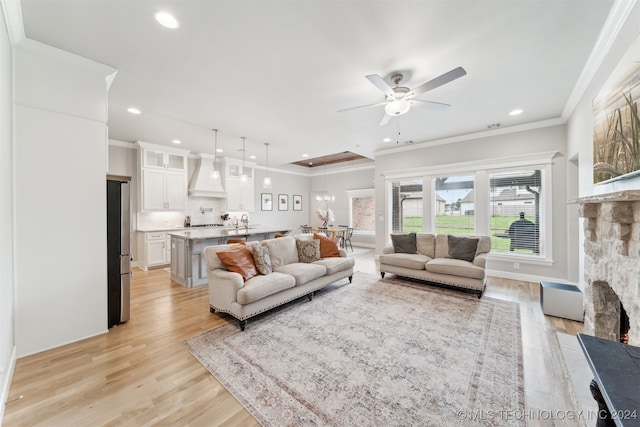 living room featuring light wood-type flooring, a stone fireplace, ornamental molding, and ceiling fan