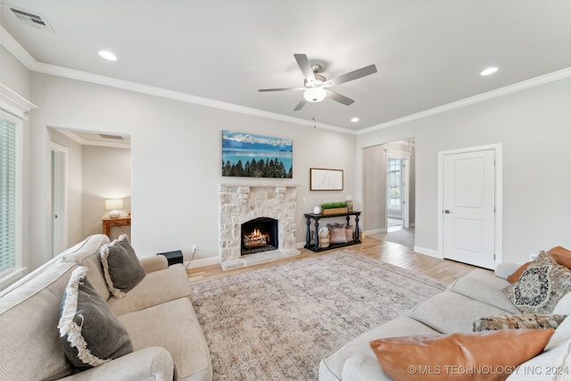 living room with ornamental molding, light hardwood / wood-style floors, ceiling fan, and a stone fireplace