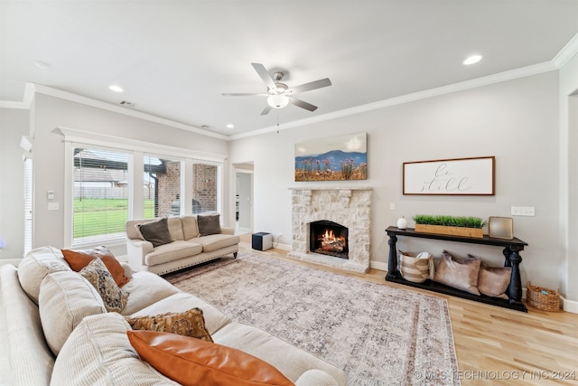 living room with wood-type flooring, a stone fireplace, crown molding, and ceiling fan