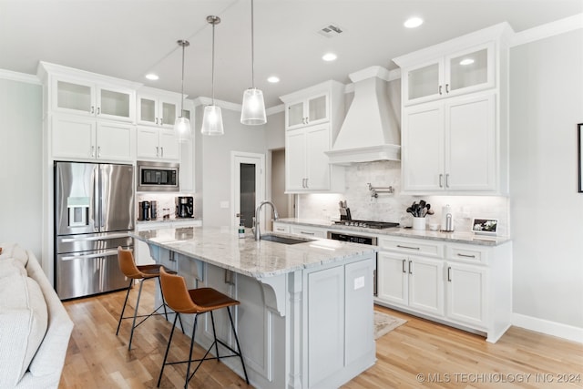 kitchen featuring premium range hood, a center island with sink, stainless steel appliances, and white cabinets