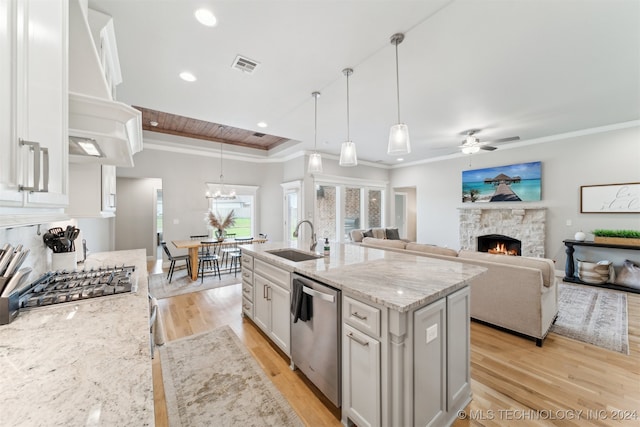 kitchen featuring light wood-type flooring, a kitchen island with sink, sink, ceiling fan with notable chandelier, and a stone fireplace