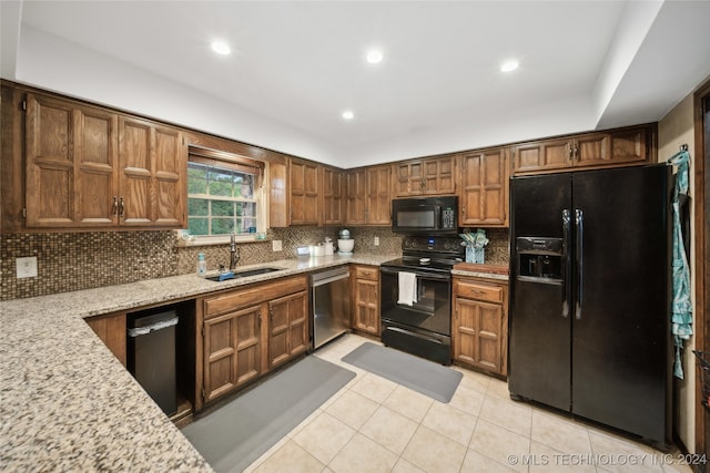 kitchen with decorative backsplash, light stone counters, light tile patterned floors, black appliances, and sink