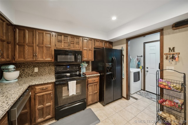 kitchen featuring decorative backsplash, light stone counters, light tile patterned floors, black appliances, and washer / dryer