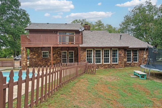 rear view of house with a lawn, a trampoline, and a fenced in pool