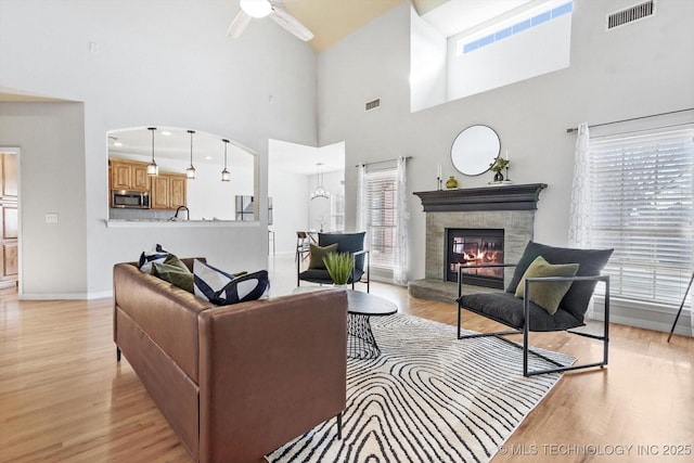 living room featuring ceiling fan, a towering ceiling, a fireplace, and light wood-type flooring