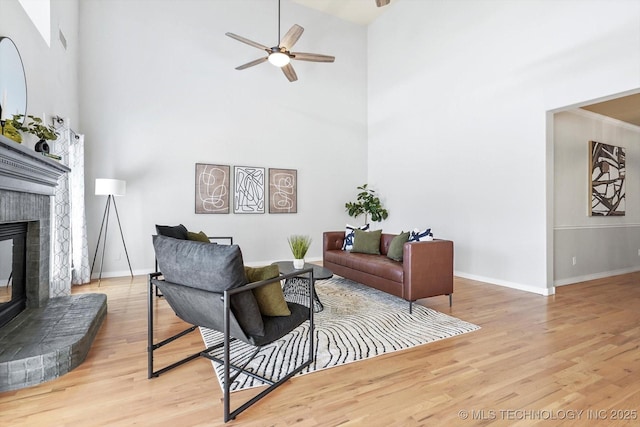 living room featuring ceiling fan, a towering ceiling, a fireplace, and light wood-type flooring