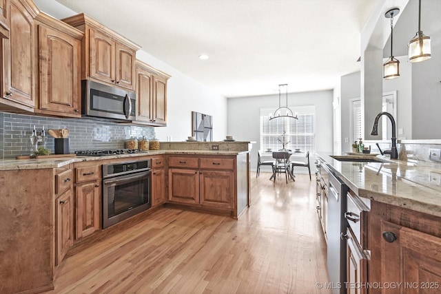 kitchen with sink, hanging light fixtures, appliances with stainless steel finishes, light hardwood / wood-style floors, and backsplash