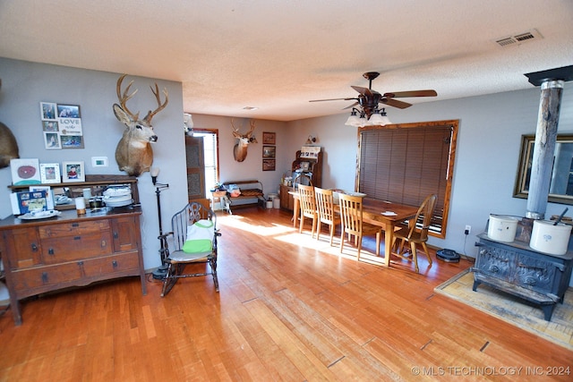 living room featuring a textured ceiling, hardwood / wood-style floors, ceiling fan, and a wood stove