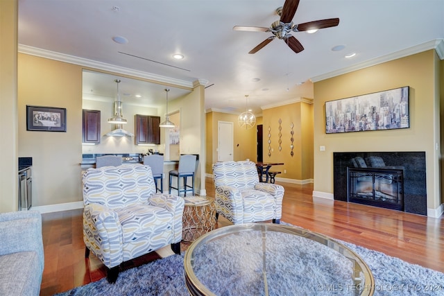 living room with wood-type flooring, ceiling fan with notable chandelier, and crown molding