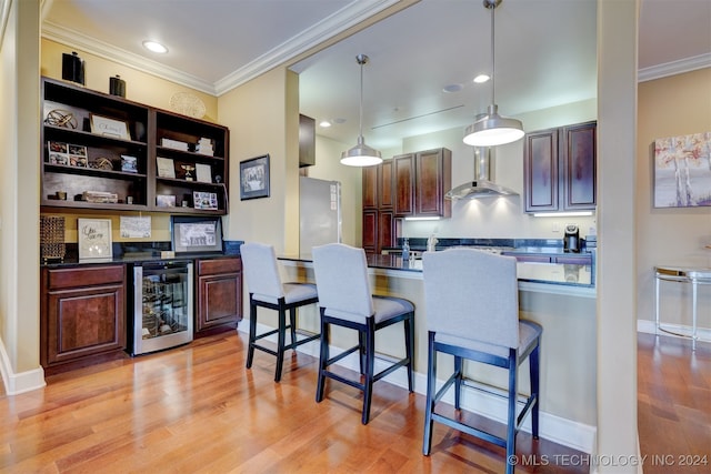 kitchen with a breakfast bar area, beverage cooler, light hardwood / wood-style flooring, decorative light fixtures, and wall chimney range hood