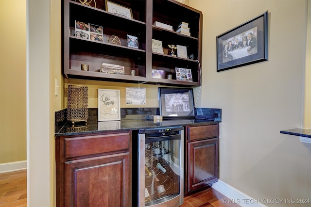 bar with dark stone counters, wine cooler, and hardwood / wood-style flooring