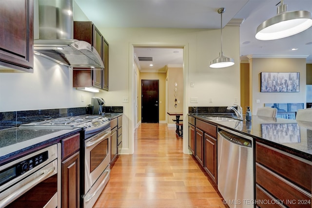 kitchen with pendant lighting, sink, wall chimney exhaust hood, appliances with stainless steel finishes, and light wood-type flooring